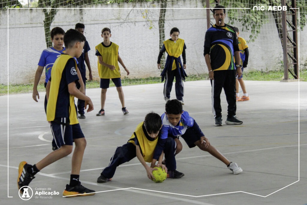Alunos do Colégio de Aplicação de Resende disputam partida de futsal durante as Olimpíadas Escolares, acompanhados pelo professor.