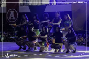 Alunos da Educacao Infantil e Ensino Fundamental se apresentando com fitas coloridas na quadra decorada durante a cerimonia de abertura das Olimpiadas Escolares 2026 no Colegio de Aplicacao de Resende.