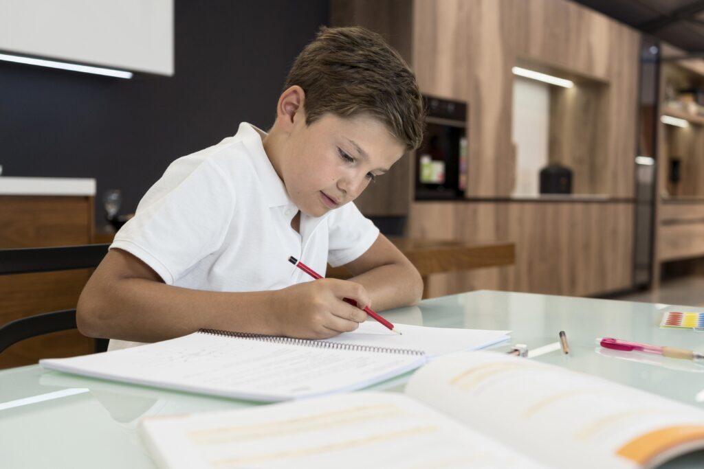 Menino concentrado fazendo a tarefa escolar do ensino fundamental com um lápis vermelho, focado na organização dos estudos e autonomia infantil.