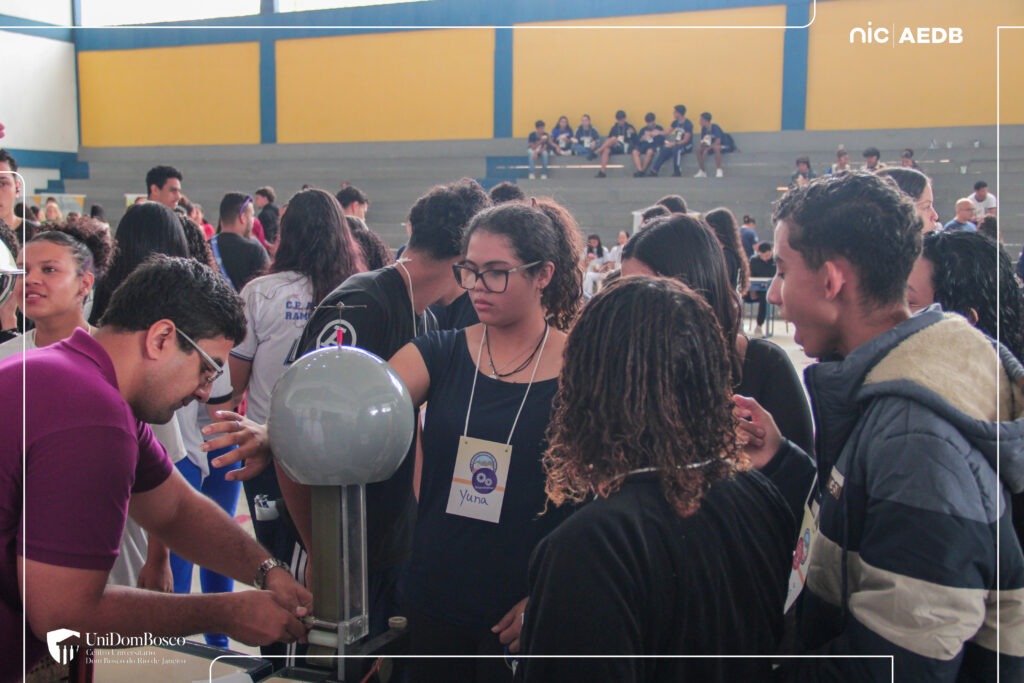 Alunos do Ensino Médio reunidos em volta de um experimento científico com gerador de Van de Graaff durante feira de profissões e orientação profissional no Colégio de Aplicação de Resende.