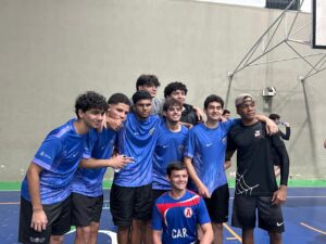 Grupo de estudantes do time masculino de futsal do Colégio de Aplicação de Resende abraçados e sorrindo na quadra esportiva durante as competições escolares do JEPAR.